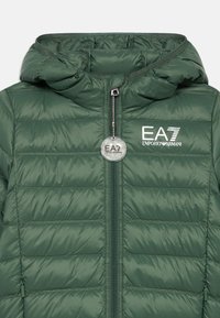 Zöld steppelt dzseki kapucnival, cipzáros záródással, varrt betétekkel és EA7 logóval a mellrészen. Díszítő kör alakú címkét tartalmaz.