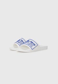 White slide sandals with a textured sole, featuring blue graphic text on a thick strap. Sleek, simplified design without additional accents.