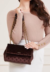 Brązowa, teksturowana torebka z klapą, złotymi łańcuszkowymi rączkami i tłoczonym logo. Materiał wydaje się miękki i o intensywnym kolorze.