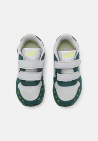 Baskets pour enfants blanches et vertes avec double bande velcro, en cuir texturé et en suède, et des détails de couture jaunes sur la semelle.