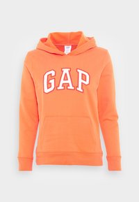 Sudadera naranja con la palabra "GAP" en blanco con contorno rojo. Incluye un bolsillo tipo canguro en la parte delantera y puños acanalados. Textura suave.