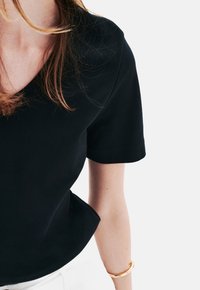Top nero a maniche corte con scollatura a V. Tessuto morbido, vestibilità rilassata con una leggera svasatura sull'orlo. Stile minimalista, senza fantasie o accenti.