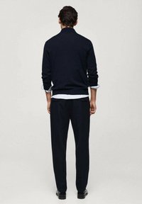 Navy knit sweater with long sleeves and ribbed hem, paired with matching dark trousers. The outfit has a minimalistic design and soft texture.