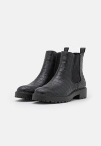 Bottes Chelsea noires avec un motif crocodile texturé, des panneaux latéraux élastiques et une semelle robuste, dotées de languettes pour un enfilage facile.