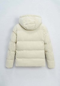 Veste matelassée en velours côtelé couleur crème, avec capuche, design matelassé et surface texturée avec des coutures horizontales visibles.