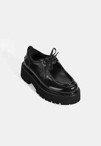 Zwarte leren schoen met een ronde neus, opvallende veters en een dikke rubberen zool met een gekarteld loopvlak. Gladde, glanzende afwerking.