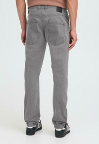 Los jeans de mezclilla gris tienen un diseño de pierna recta, dos bolsillos traseros y una etiqueta negra en la cinturilla. La tela tiene una textura suave.