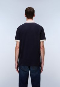 Μπλε μπλούζα πόλο με αντίθετο, εκρού γιακά και περιθώριο στα μανίκια. Κοντά μανίκια, βαμβακερό υλικό, άνετη εφαρμογή, φορεμένη με σκούρο τζιν.