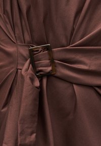 Σκούρο καφέ ύφασμα που μαζεύεται και περαστεί μέσα από ένα ορθογώνιο αγκράφα σε σχέδιο χελώνας στο κέντρο.