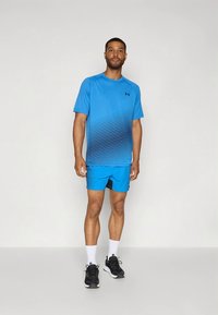 Lyseblått treningsskjorte med et gradientmønster, kombinert med matchende blå shorts med teksturerte detaljer, svart utstyr og hvite sokker.