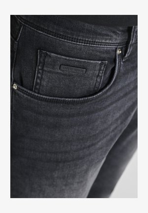 Nahaufnahme einer schwarzen Denim-Jeans vorne mit einer kleinen Armbanduhr und einem Etikett mit der Aufschrift Antony Morato.