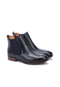 Bottes Chelsea en cuir noir avec des panneaux élastiques sur les côtés, bout arrondi et petit talon empilé. L'intérieur présente une doublure beige et des languettes à l'arrière.