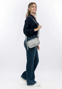 Borsa a tracolla in pelle grigia chiara con dettaglio del bordo intrecciato, dotata di una lunga tracolla, su uno sfondo bianco semplice.