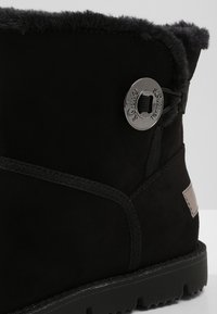 Bottine en daim noir avec col en fausse fourrure, détail en métal argenté rond, accents cousus et semelle en caoutchouc texturée.