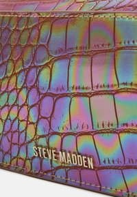 Borsa iridescente viola con texture a coccodrillo. Presenta squame in rilievo e cuciture visibili; include il logo "STEVE MADDEN" in lettering metallico.
