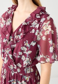 Bordeaux bloemenjurk met een volanthalslijn en mouwen, elastische taille, gemaakt van lichtgewicht stof, met witte en gele bloempatronen.