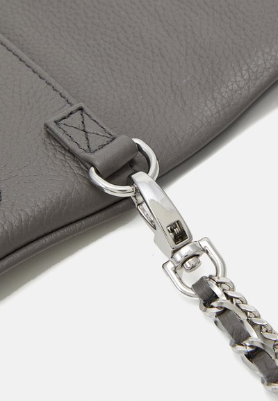 Coin du sac en cuir gris montrant un fermoir en métal argenté et une bandoulière en chaîne, avec une surface texturée et des détails de couture sur le cuir.