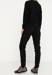 Svart idrotts sweatshirt och byxor, med en avslappnad passform, ribbad manschett och texturerad tyg. Sportskor med rosa detaljer.