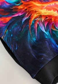 Nahaufnahme eines Stoffes mit lebendigen, feuerscharfen orange-blauen abstrakten flammenartigen Mustern, eingefasst von einem schwarzen gerippten Strickbündchen.