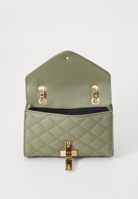 Borsa a tracolla in ecopelle verde trapuntata con un flap esagonale, hardware dorato, due ganci metallici e una tasca interna con zip nera.