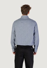 Camicia button-up azzurro chiaro e testurizzata con maniche lunghe, vista posteriore, abbinata a pantaloni neri, con colletto e polsini abbottonati.