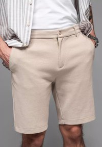 Pantalones cortos beige de tejido texturizado, con una cintura que cuenta con un botón y cierre de cremallera, bolsillos laterales y dobladillos enrollados.
