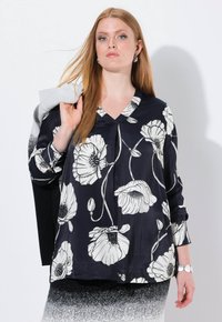 Merineule sininen paita, jossa on suuri valkoinen kukkakuosi, V-pääntie, pitkät hihat ja kevyt kangas. Mallilla on harmaa esine olkapäänsä yli.