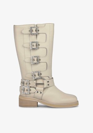 Stivale in pelle beige alto fino al ginocchio con quattro fibbie decorative arricchite da strass, una fascia larga con una fibbia circolare e un tacco in legno spesso.