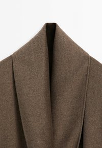 Close-up of a brown wool coat collar with a wide, shawl lapel on a plain white background.