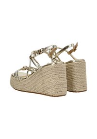 Sandalias doradas metálicas con tiras y tacones de cuña de esparto; textura tejida en beige en la suela y correa ajustable en el tobillo.