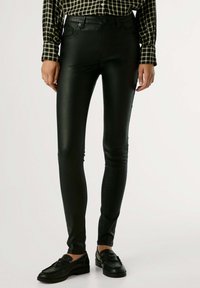 Pantalones ajustados de imitación de cuero negros con diseño clásico de cinco bolsillos y un brillo sutil, combinados con una camisa de cuadros y mocasines negros.