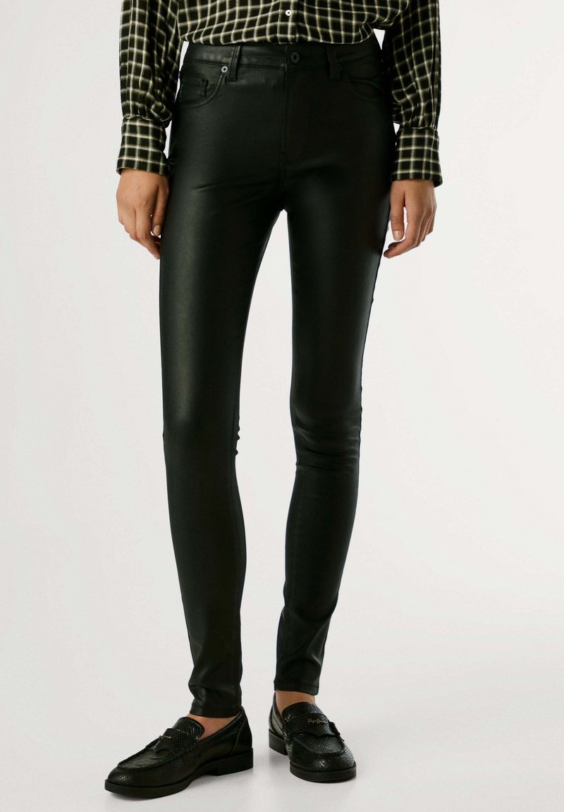 Pantalones ajustados de imitación de cuero negros con diseño clásico de cinco bolsillos y un brillo sutil, combinados con una camisa de cuadros y mocasines negros.