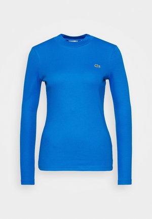Bright blue long-sleeve fitted crewneck shirt with small green crocodile logo on the left chest against a plain background.