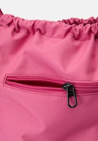 Saco de cordão rosa feito de um tecido texturizado e resistente a rasgos. Apresenta um pequeno bolso com fecho por zíper e um puxador preto na parte da frente para armazenamento seguro.