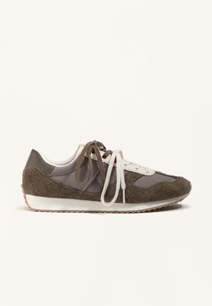 Barna és szürke színű velúr és nejlon sportcipő fehér és barna fűzőkkel, fehér talppal és texturált gumi külső talppal, oldalnézetben, fehér háttéren.