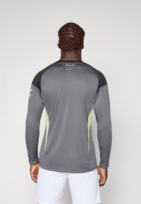 Langärmliges Sportshirt in Grau mit schwarzen Schulterakzenten und neon-grünen Seiteneinsätzen. Hergestellt aus glattem, leichtem Material.