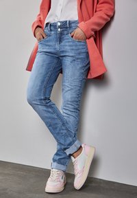 Vaaleansiniset farkut, joissa on slim fit -malli, kahdella etutaskulla ja käännetyillä lahkeilla, yhdistettynä valkoisiin ja vaaleanpuniisiin tennareihin.