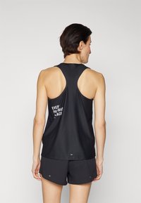 Débardeur de sport noir avec un design dos nageur. Présente un texte blanc au dos. Associé à un short noir, les deux en matériau léger.
