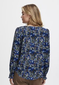 Blusa a maniche lunghe con un motivo floreale blu su sfondo nero, dalla vestibilità ampia e dettagli arricciati sulle spalle.