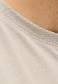 Beige bomuld t-shirts stof tæt på, med en ribbet rund halsudskæring og glat tekstur, med synlige syningsdetaljer.