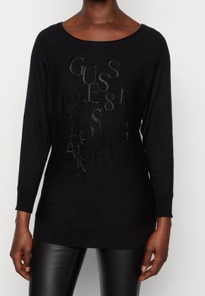 Pull noir à manches longues avec un col large. Présente un texte en relief et scintillant, "GUESS 81" et "LOS ANGELES." Matière en tricot douce.