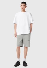 Άσπρο βαμβακερό T-shirt με άνετη εφαρμογή, συνδυασμένο με γκρι σορτς που έχουν εκτύπωση λογότυπου και μαύρ α δερμάτινα παπούτσια με κορδόνια και χοντρές σόλες.