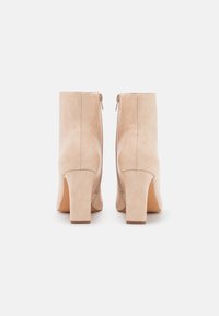 Bottines en cuir beige à texture lisse, talons carrés épais, avec fermetures éclair latérales, présentant un design minimaliste et des lignes épurées.
