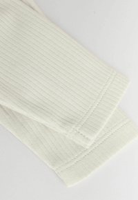 Ljusbeige ribbat stickat tyg med en slät yta, med prydlig sömnad och avslutade kanter, som framhäver plaggets form och design.