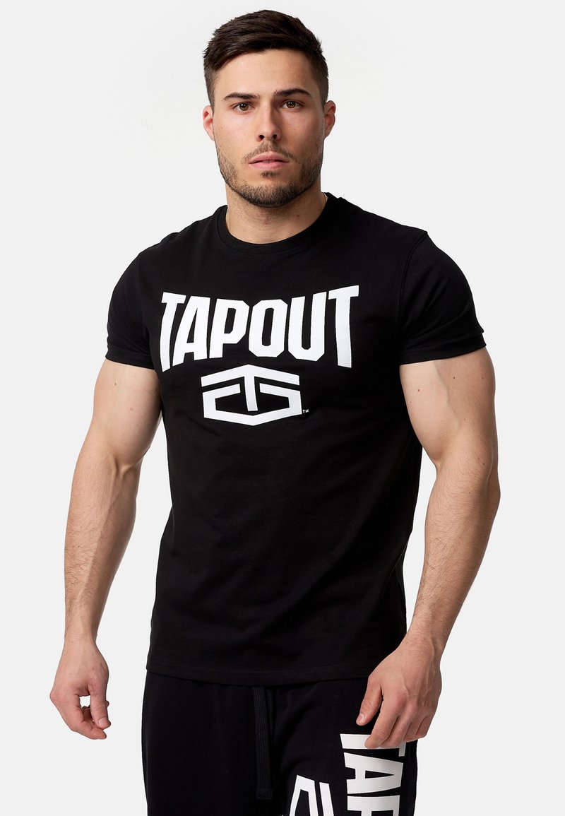 Melns kokvilnas T-krekls ar lielu baltu „TAPOUT” logo priekšpusē. Redzami īsie piedurknes un klasiskā apaļā kakla izgriezums.