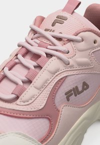 Baskets FILA roses et beiges avec lacets blancs, panneaux latéraux texturés et logos de la marque sur la languette et le côté extérieur.