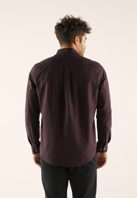 Long-sleeve, dark purple shirt made of smooth fabric. Features buttoned cuffs and a back pleat for improved fit.