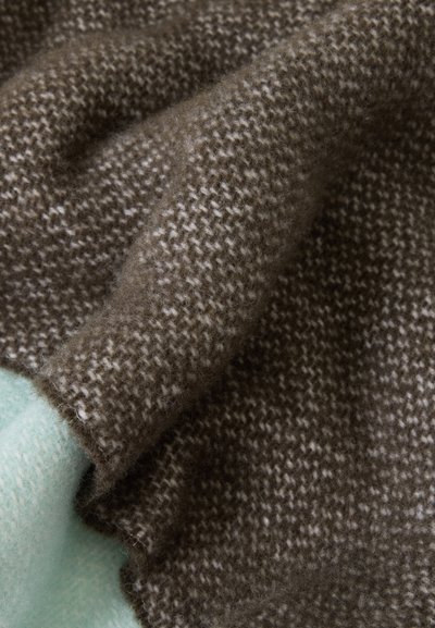 Gros plan d'un tissu tricoté doux, tacheté de brun et de blanc, plié sur un matériau texturé bleu clair en dessous.