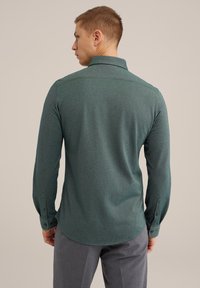 Camisa verde de manga larga hecha de una tela texturizada. Presenta un cuello puntiagudo y puños abotonados, con un dobladillo redondeado y un corte ajustado.