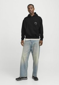 Zwarte hoodie met witte bedrukt logo, relaxte pasvorm, gecombineerd met lichtblauwe baggy jeans en zwarte sneakers. Eenvoudig, casual ontwerp.